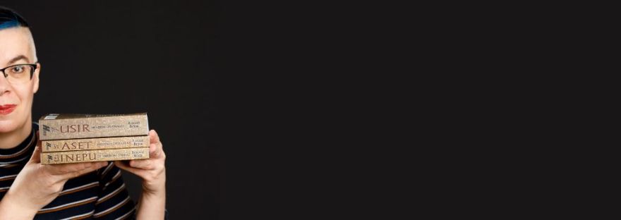 Roxane hält die drei Bücher Inepu, Aset und Usir in der Hand